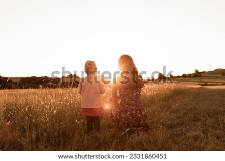 Mother and child bonding in a field at sunset, surrounded by nature's beauty.