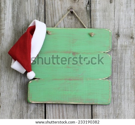 Blank wood holiday sign with Christmas Santa Claus hat hanging on antique rustic wooden background; Christmas background with green copy space