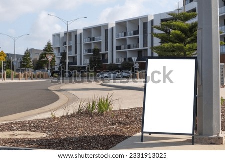 Blank white mockup background texture of a sandwich marketing advertisement signage board placed outdoor on urban roadside with some residential apartments in the distance. Copy space for your design.