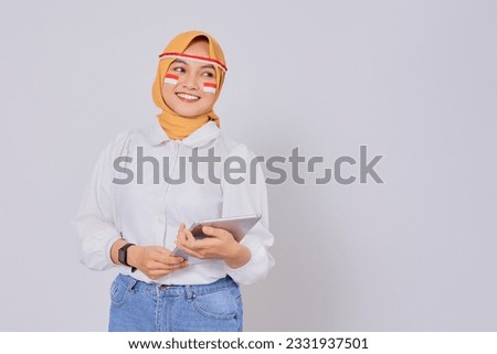Smiling happy young Asian Muslim woman wearing a hijab holding a digital tablet isolated over white background. Celebrate Indonesian independence day on 17 August