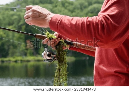 a closeup of a man fishing after catching a string of sea weed on a sunny summer day Royalty-Free Stock Photo #2331941473