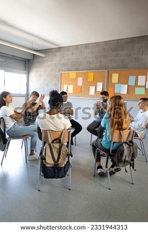 Multiracial high school students sitting in a circle clapping together celebrating achievement. Support group. Vertical.