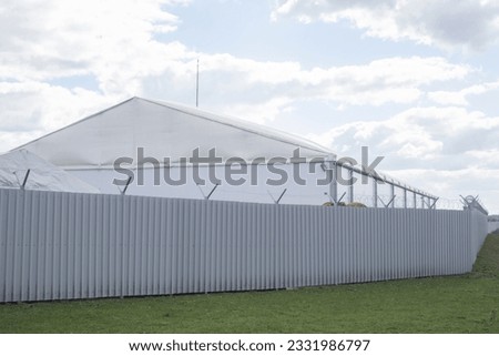 White industrial building. Steel fence along territory. Fence around industrial zone. Warehouse building.