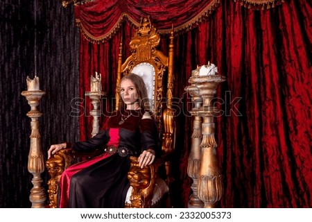 Lovely lady in an old style on antique throne fortress, looking at camera. Medieval queen in historical image posing sitting on golden throne in castle room. Concept of theatrical. Copy ad text space Royalty-Free Stock Photo #2332005373