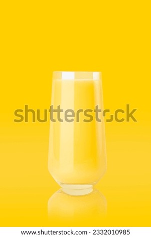 Yellow orange juice in glass with reflection on colorful yellow background, copy space, vertical. Fresh summer healthy citrus beverage for advertise, poster, card, design.