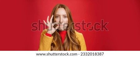 Girl putting seal on mouth making promise not tell anyone secret, sucking lips and holding finger near as zipping not spill words, looking serious and determined to keep surprise safe over red wall.