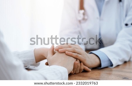 Doctor and patient sitting at the wooden table in clinic. Female physician's hands reassuring woman. Medicine concept Royalty-Free Stock Photo #2332019763