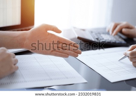 Woman accountant using a calculator and laptop computer while counting and discussing taxes with a client. Business audit concepts