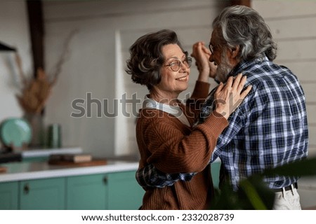 Happy elderly couple is laughing and dancing in the kitchen on their anniversary day. Old couple have emotional dance while listening good music