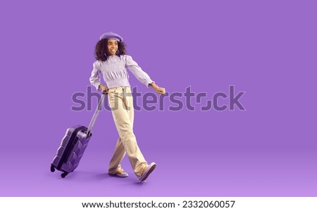 Joyful dark-skinned teenage girl in stylish clothes and with suitcase is ready for vacation trip. Curly kid girl in beret goes with suitcase for travel on purple background. Full length. Web banner.