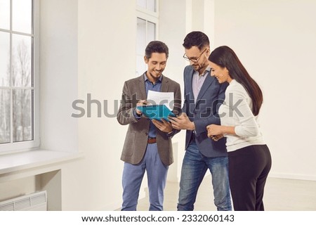 Young happy smiling couple reaching agreement with realtor and looking through the contract of real estate sale going to sign a deal. Family ready to become homeowners. Real estate market concept. Royalty-Free Stock Photo #2332060143