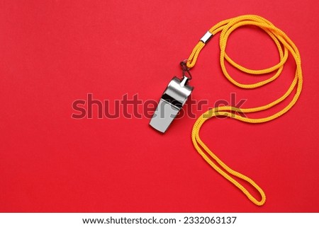One metal whistle with cord on red background, top view. Space for text Royalty-Free Stock Photo #2332063137