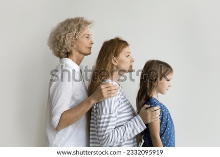 Girls and women of three female generations side portrait. Serious grandma, mom and kid standing in row, touching shoulders, expressing family support to each other