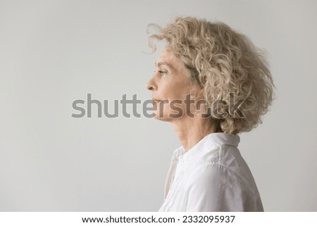 Thoughtful serious pretty blonde mature woman standing at white studio background, looking away in deep thoughts. Beautiful senior model wir curly fair hair side portrait Royalty-Free Stock Photo #2332095937