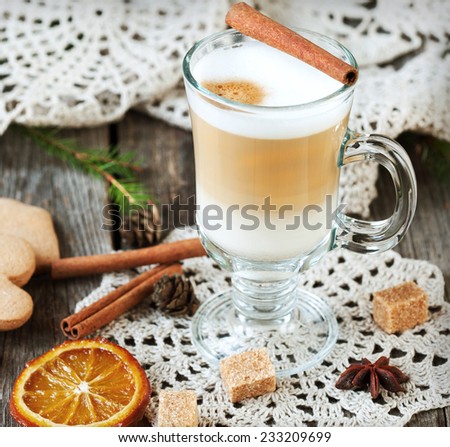 Hot coffee with milk in a glass on a wooden table with pieces of sugar, cinnamon sticks and candied orange slice. Selective focus, toned