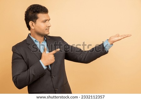 Happy young indian businessman wearing suit pointing at blank space isolated over beige background. Look here, Advertisement and promotion.