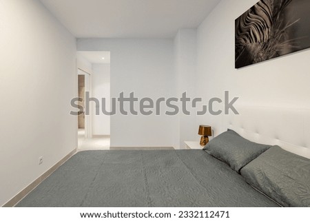 Bedroom with an open door with a double bed and a bedside table with stylish gray linens and a picture on the wall in a bright compact bedroom. The concept of concise apartment design