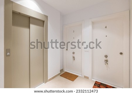 Hall space with a passenger lift and hotel rooms with the numbers three and four in white. The concept of a cozy modern apartment building Royalty-Free Stock Photo #2332112473