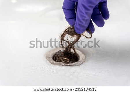 hand in a purple rubber glove pulls hair out of the shower drain Royalty-Free Stock Photo #2332134513