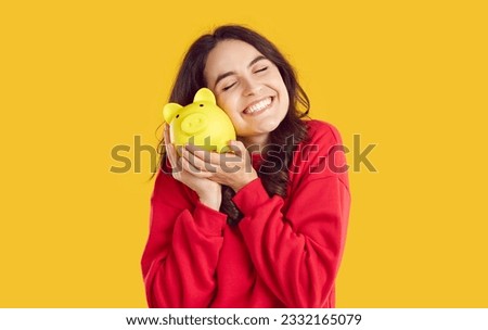 Portrait of happy smiling brunette woman snuggling up to yellow piggy bank on yellow background with closed eyes. She is happy about her savings. Saving money, self finance, savings, capital concept. Royalty-Free Stock Photo #2332165079