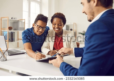 Happy family signing contract after consulting with real estate agent or mortgage broker. Mixed race couple at office desk together putting signatures on contract of sale or notary rent agreement