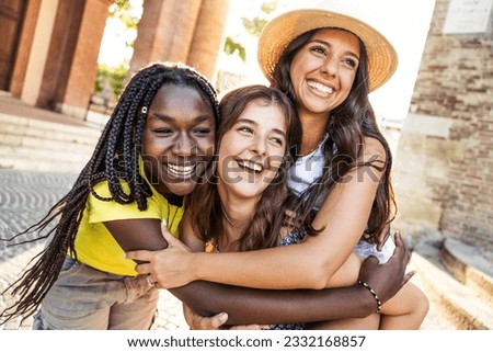 Three young multicultural women having fun together on city street - Happy female tourists enjoying summer vacation outside - Best friends hugging together - Friendship and life style concept