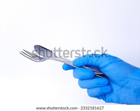 A hand with white latex glove holds metal spoon and fork. Isolated on a white background