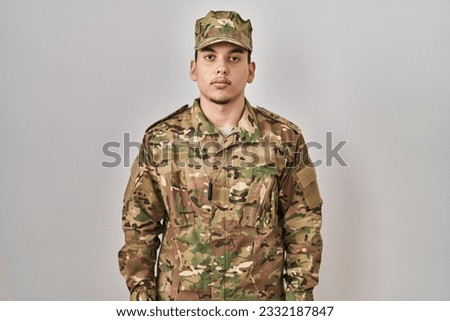 Young arab man wearing camouflage army uniform relaxed with serious expression on face. simple and natural looking at the camera. 