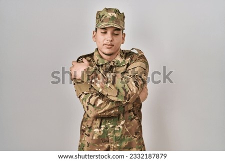 Young arab man wearing camouflage army uniform hugging oneself happy and positive, smiling confident. self love and self care 