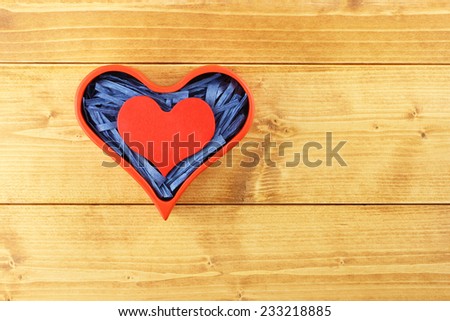 Red painted wooden heart enclosed with blue paper raffia strips in box isolated on wooden background