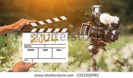 2024 - handwritten on film clapperboard. film crew holding film clapperboard and a camera filming a movie in the outdoor background. for creator content in new year 2024