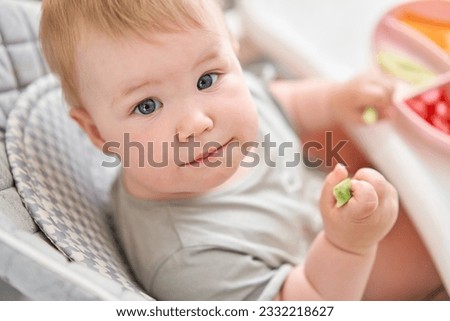 Cute child eats healthy food pasta and vegetables steamed,. Portraits of a cute 10 months old baby girl. The baby sitting in a special high chair for babies.  Royalty-Free Stock Photo #2332218627