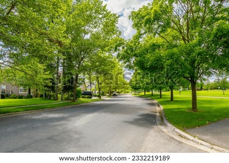A shady tree lined street in a subdivision of homes across from a park in the suburban city of Coeur d'Alene, Idaho USA. Royalty-Free Stock Photo #2332219189