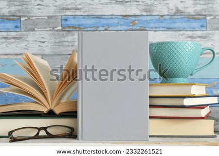 Book cover mock up - plain book against stacks of books with mug and glasses.