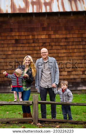 Family lifestyle portrait of a mother, father, son and daughter in front of a rustic barn in the country.