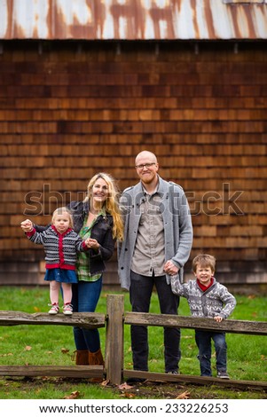 Family lifestyle portrait of a mother, father, son and daughter in front of a rustic barn in the country.