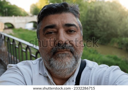 young adult man with beard taking a selfie as a souvenir on the river bank and a bridge