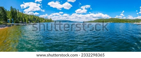 Panoramic view from the public beach of waterfront homes, marina and the mountains surrounding Carlin Bay, one of the bays on Lake Coeur d'Alene, in Coeur d'Alene, Idaho, in the North Idaho Panhandle. Royalty-Free Stock Photo #2332298365
