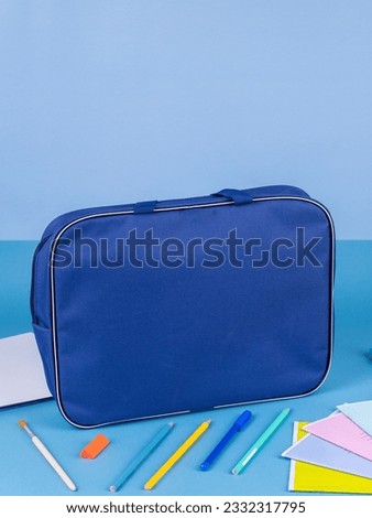 Blue  briefcase folder for documents and school items on a bright blue table next to stationery