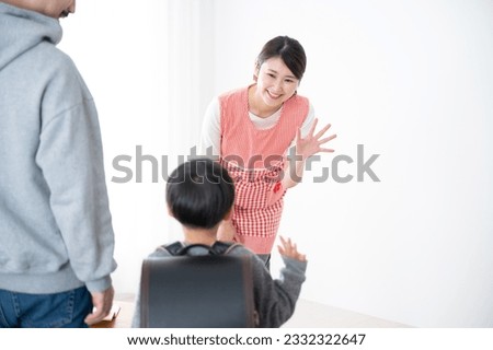 Image of a Japanese female teacher seeing off or picking up her student's children at home, kindergarten, daycare center, or school. Royalty-Free Stock Photo #2332322647