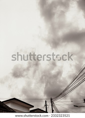 the view of the sky behind the buildings lined with cables and street poles. The picture was taken in the evening when the weather was getting dark and cloudy