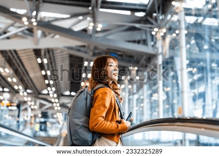 Young asian woman in international airport terminal or modern train station. Backpacker passenger female commuter walking on escalator Royalty-Free Stock Photo #2332325289