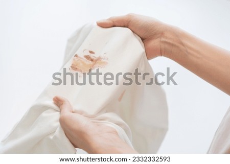 Housewife, asian young maid woman hand in holding white shirt, showing making cloth stain, spot dirty or smudge on clothes, dirt stains for cleaning before washing, making household working at home. Royalty-Free Stock Photo #2332332593