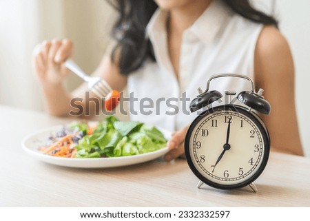 Intermittent fasting with clock, health asian young woman, girl weight loss, eating green fresh vegetable salad on dish, plate with eat healthy of breakfast food in morning, lunch on a table at home. Royalty-Free Stock Photo #2332332597