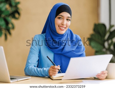 beautiful young smiling muslim woman in traditional religious hijab works remotely on laptop from home