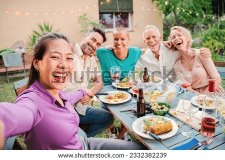 Group of mature adult friends smiling taking a selfie on a barbeque party celebration at home backyard. Middle age people shooting pictures sitting at patio table with positive and friendly expression