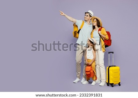 Traveler parents mom dad with child girl wear casual clothes hold bags point aside isolated on plain purple background. Tourist travel abroad in free time rest getaway. Air flight trip journey concept