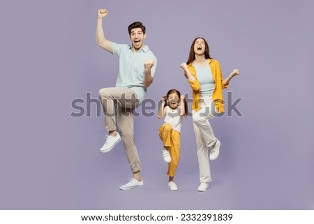 Full body young parent mom dad with child kid daughter girl 6 years old wear blue yellow casual clothes do winner gesture celebrate raise up leg isolated on plain purple background. Family day concept