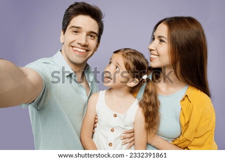 Close up fun young parents mom dad with child kid daughter girl 6 year old wear blue yellow casual clothes do selfie shot pov mobile cell phone isolated on plain purple background Family day concept