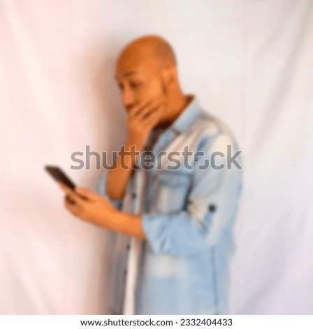 Blurry image of shocked young bald man covering his mouth while reading bad news on smartphone 
